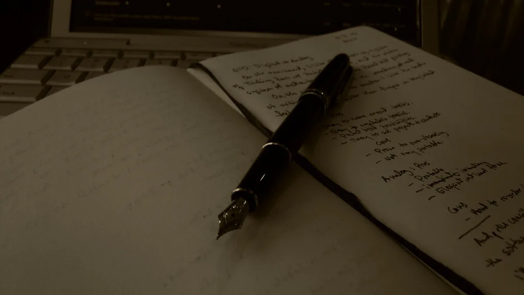 A notebook of handwritten notes beside a fountain pen